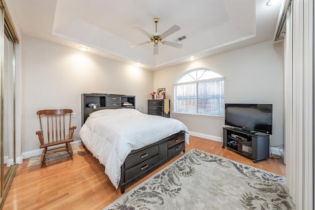 bedroom featuring a closet, light wood-type flooring, a tray ceiling, and ceiling fan