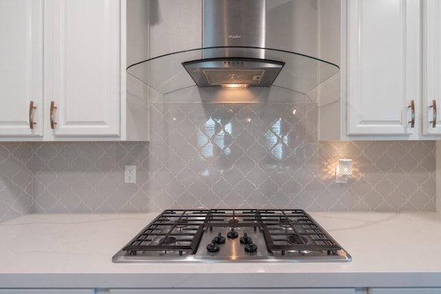 kitchen featuring stainless steel gas cooktop, backsplash, ventilation hood, light stone countertops, and white cabinetry