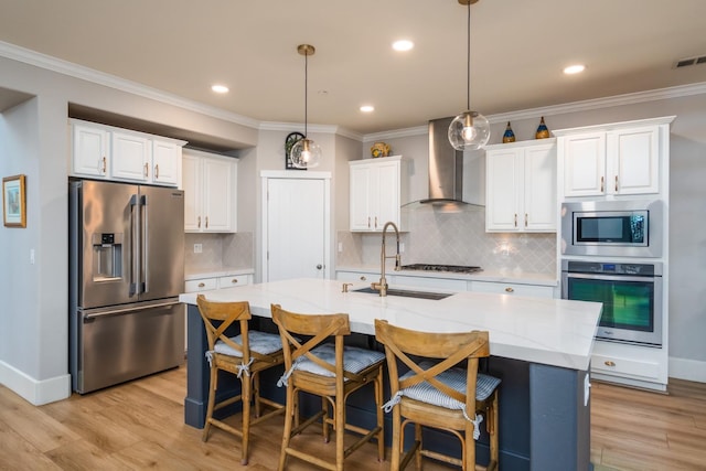 kitchen with a center island with sink, appliances with stainless steel finishes, white cabinetry, wall chimney exhaust hood, and sink