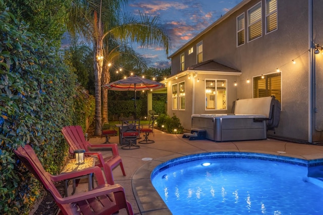 pool at dusk featuring a hot tub and a patio area