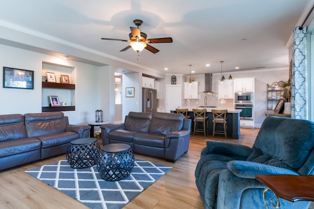 living room with ornamental molding, sink, light wood-type flooring, and ceiling fan