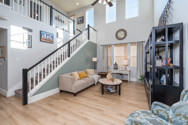 living room with light hardwood / wood-style floors, ceiling fan, and a towering ceiling