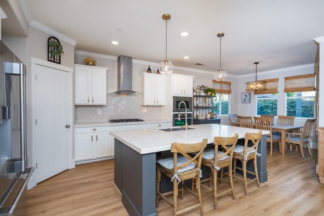 kitchen with wall chimney range hood, white cabinetry, and a center island with sink