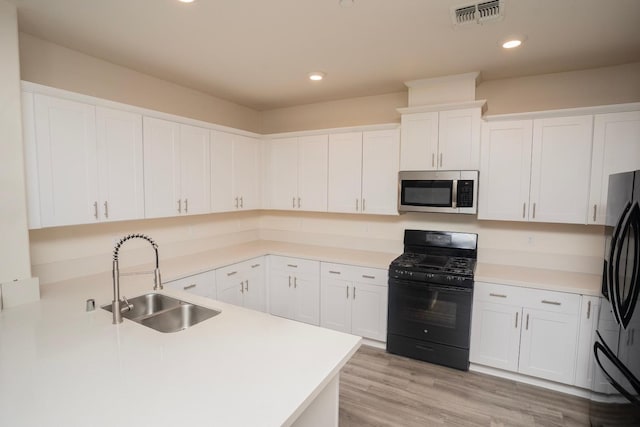 kitchen with sink, black appliances, light hardwood / wood-style floors, and white cabinets