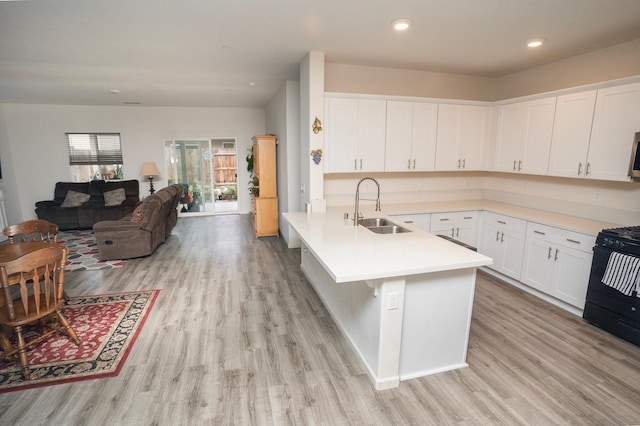 kitchen featuring black range with gas cooktop, sink, white cabinetry, light wood-type flooring, and a kitchen breakfast bar