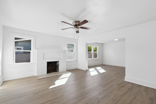 unfurnished living room featuring baseboards, a ceiling fan, wood finished floors, and a fireplace