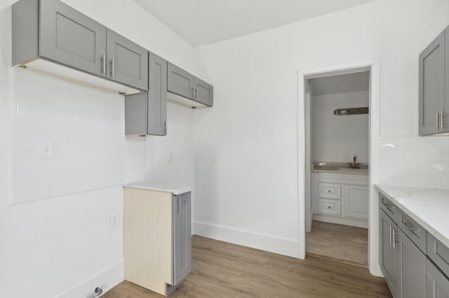 kitchen with light stone counters, a sink, light wood-type flooring, gray cabinets, and baseboards