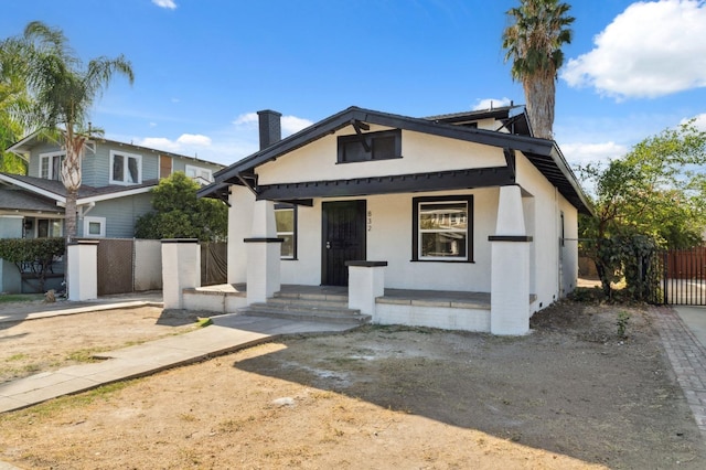 bungalow with stucco siding, covered porch, a chimney, and fence