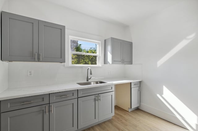 kitchen with decorative backsplash, light stone countertops, light hardwood / wood-style flooring, gray cabinetry, and sink