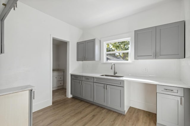 kitchen featuring gray cabinets, tasteful backsplash, a sink, and light wood finished floors