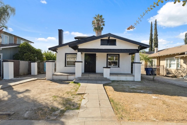 view of front of house featuring stucco siding, a gate, fence, and covered porch