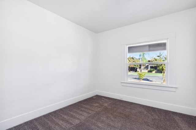 spare room featuring dark colored carpet and baseboards