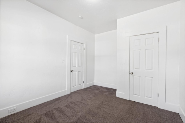 spare room featuring dark carpet and baseboards