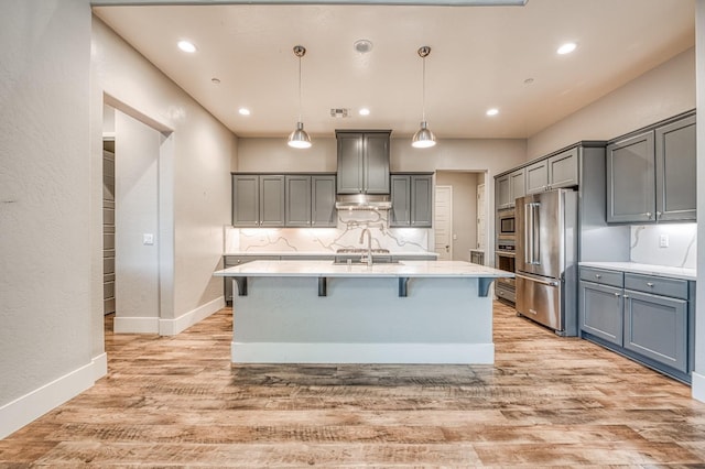 kitchen featuring under cabinet range hood, gray cabinetry, light countertops, and appliances with stainless steel finishes