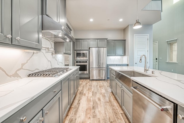 kitchen featuring a sink, stainless steel appliances, gray cabinets, light wood-type flooring, and decorative backsplash