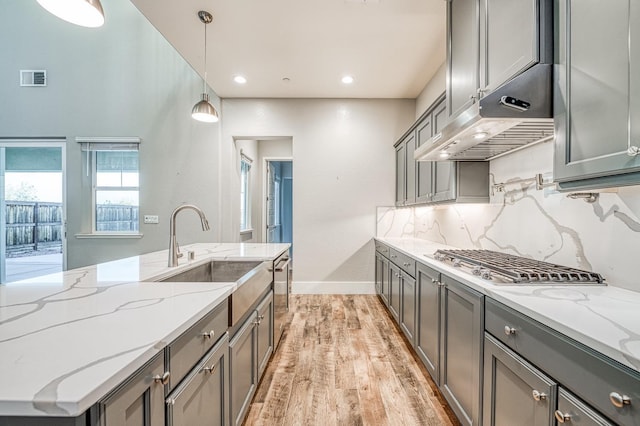kitchen featuring a sink, gray cabinets, under cabinet range hood, light wood finished floors, and baseboards