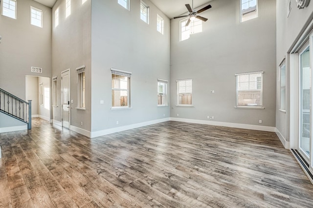 unfurnished living room with stairs, wood finished floors, a ceiling fan, plenty of natural light, and a high ceiling