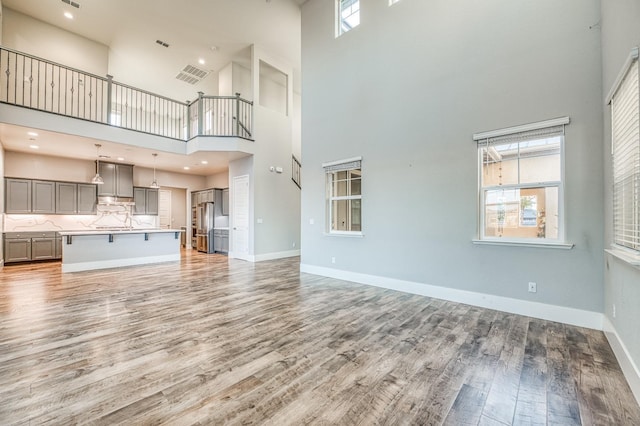unfurnished living room with baseboards, visible vents, light wood-type flooring, and a high ceiling