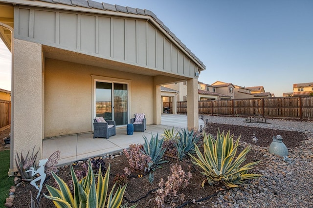 rear view of house with board and batten siding, a patio, stucco siding, and a fenced backyard