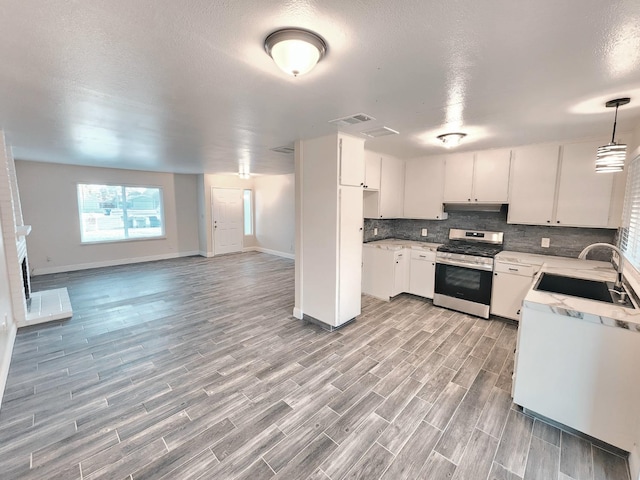 kitchen featuring sink, light wood-type flooring, hanging light fixtures, white cabinetry, and stainless steel stove