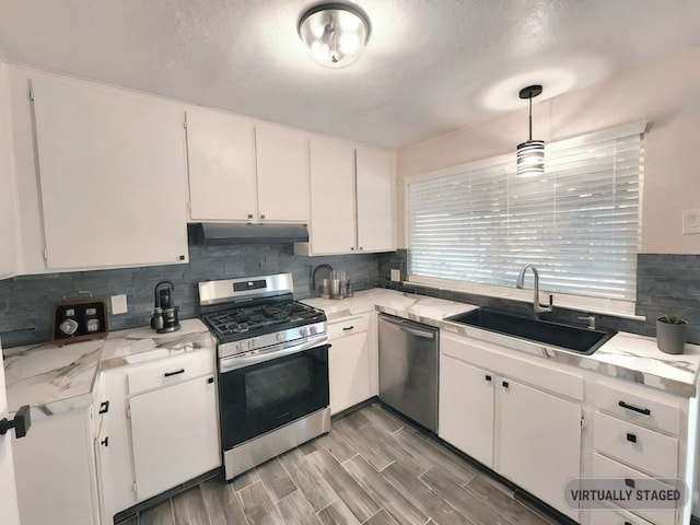 kitchen featuring white cabinetry, light wood-type flooring, sink, decorative light fixtures, and stainless steel appliances