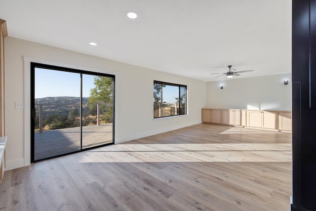 unfurnished living room with ceiling fan, light wood-type flooring, and a wealth of natural light