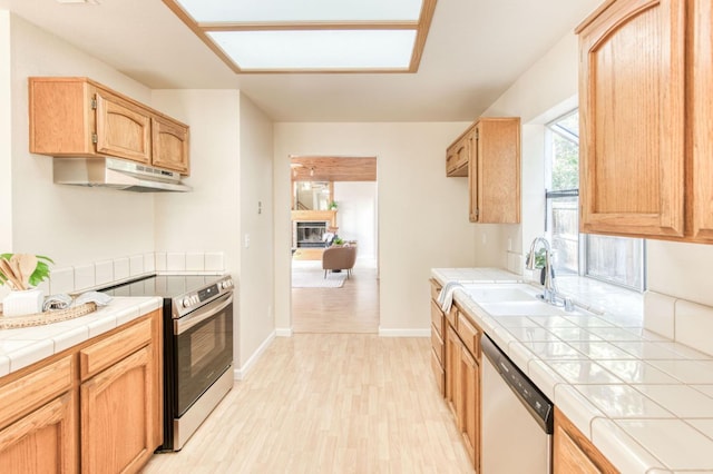 kitchen featuring sink, appliances with stainless steel finishes, tile counters, and light wood-type flooring