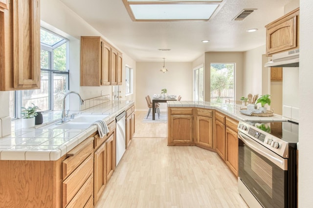 kitchen featuring tile countertops, exhaust hood, appliances with stainless steel finishes, light hardwood / wood-style floors, and a skylight