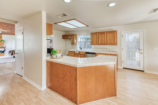 kitchen with light hardwood / wood-style flooring, kitchen peninsula, tile counters, and dishwasher