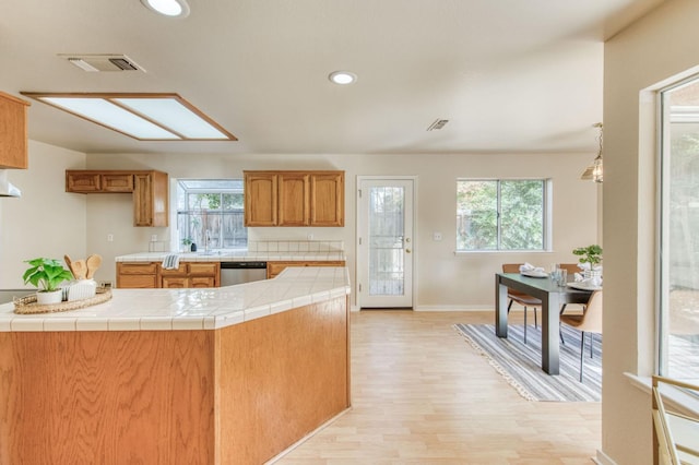 kitchen featuring dishwasher, tile counters, light wood-type flooring, and plenty of natural light