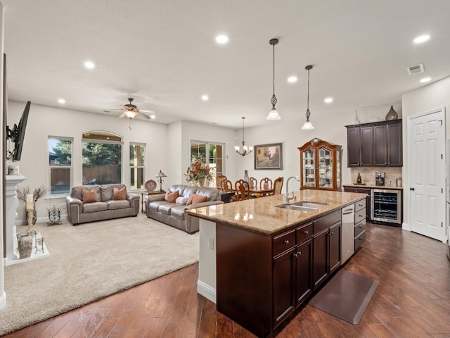 kitchen with decorative light fixtures, an island with sink, sink, beverage cooler, and dark brown cabinets