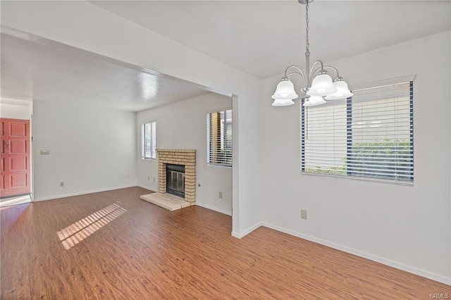 49400 River Park Rd Unit 17, Oakhurst, CA 93644 - unfurnished living room with a chandelier, wood finished floors, a brick fireplace, and baseboards
