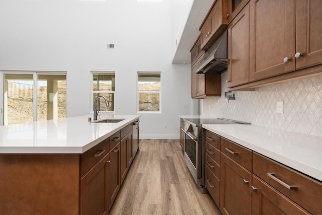 kitchen featuring high end stainless steel range oven, sink, light hardwood / wood-style floors, decorative backsplash, and a kitchen island with sink