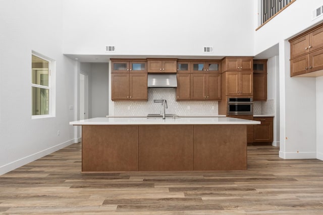 kitchen featuring oven, dark hardwood / wood-style flooring, decorative backsplash, exhaust hood, and a kitchen island with sink