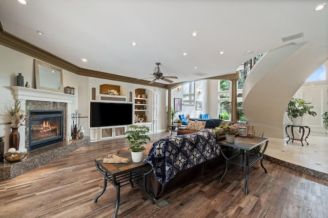 living room with hardwood / wood-style floors, built in shelves, ceiling fan, a fireplace, and ornamental molding