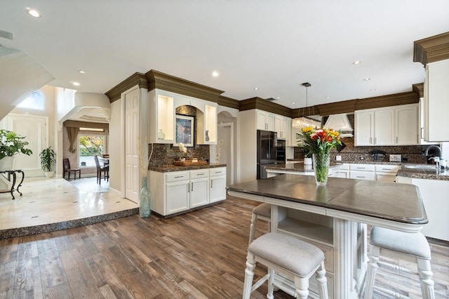 kitchen with black fridge, white cabinets, custom exhaust hood, and hanging light fixtures