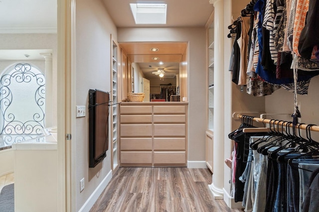 spacious closet featuring a skylight, ceiling fan, and light hardwood / wood-style flooring