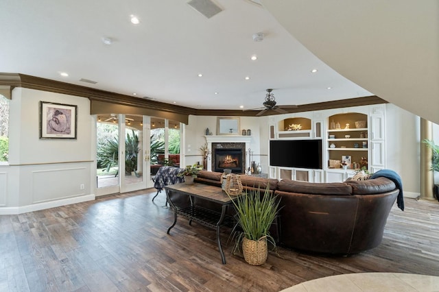 living room with ornamental molding, ceiling fan, hardwood / wood-style flooring, built in features, and a premium fireplace