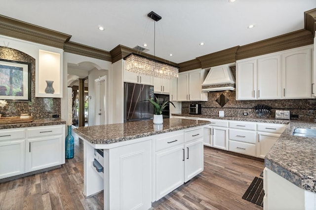 kitchen featuring a center island, white cabinetry, custom range hood, hanging light fixtures, and stainless steel fridge