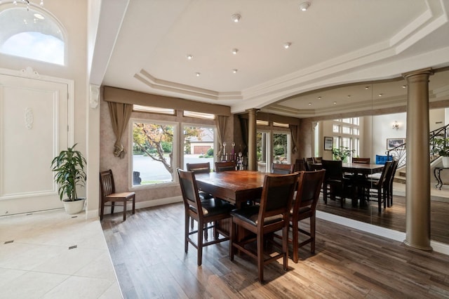 dining area with a tray ceiling, wood-type flooring, and ornate columns