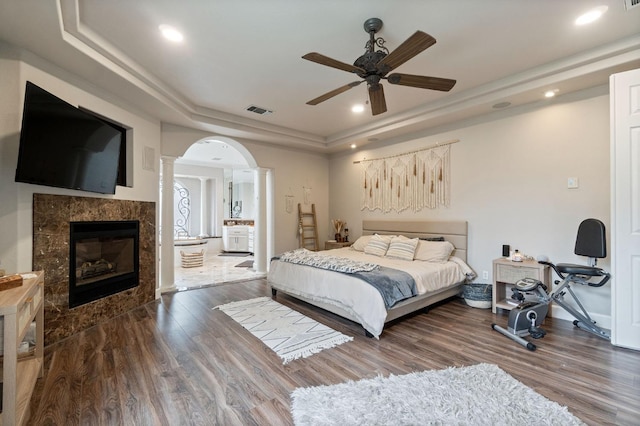 bedroom featuring a raised ceiling, ornate columns, ceiling fan, a fireplace, and hardwood / wood-style flooring