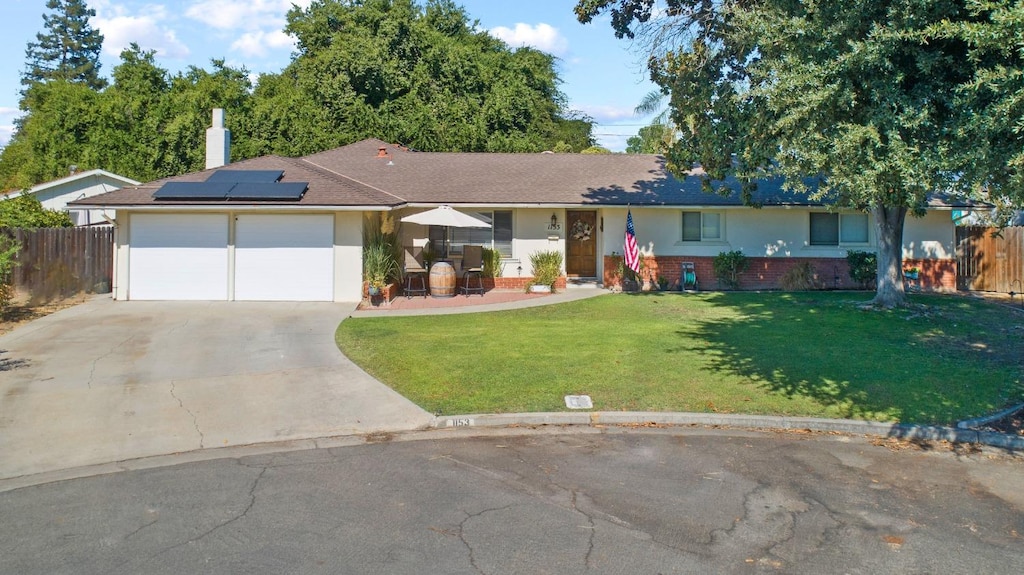 ranch-style house featuring a garage, a front lawn, and solar panels