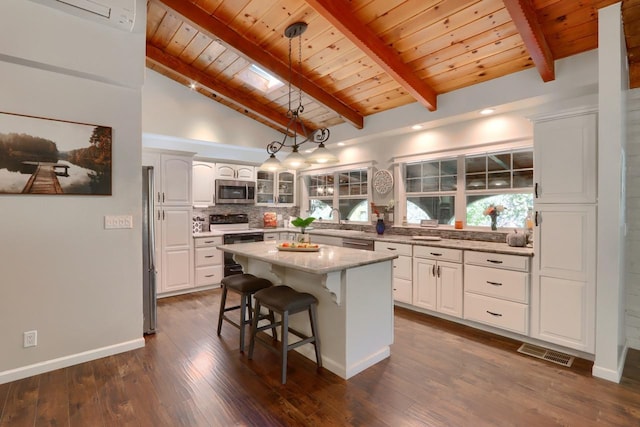 kitchen with appliances with stainless steel finishes, decorative light fixtures, a center island, wooden ceiling, and beam ceiling