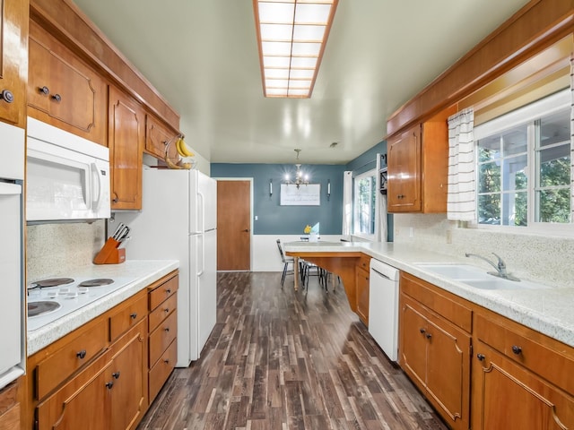 kitchen with a chandelier, light countertops, dark wood finished floors, white appliances, and brown cabinetry