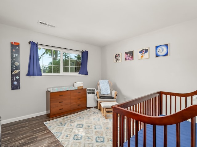 bedroom featuring visible vents, a nursery area, dark wood-style flooring, and baseboards