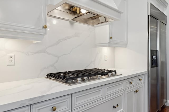 kitchen with custom exhaust hood, light stone counters, backsplash, white cabinetry, and stainless steel appliances