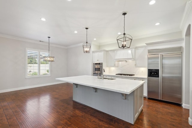 kitchen with dark wood-type flooring, a center island with sink, appliances with stainless steel finishes, white cabinetry, and premium range hood