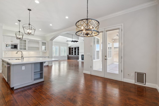 kitchen featuring dark hardwood / wood-style flooring, stainless steel microwave, decorative light fixtures, and an island with sink