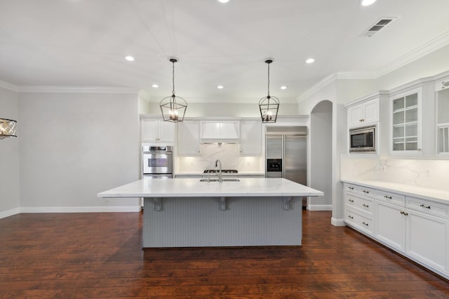 kitchen featuring built in appliances, an island with sink, and dark hardwood / wood-style flooring