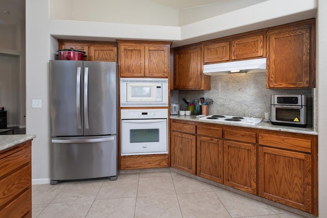 kitchen with white appliances, decorative backsplash, brown cabinets, light countertops, and under cabinet range hood